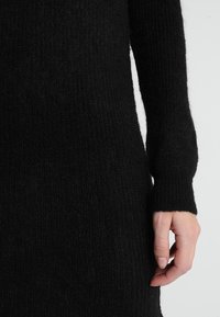 Pull en maille noire avec une finition texturée, doté de manches longues et d'une coupe décontractée. Le tissu semble doux et confortable.