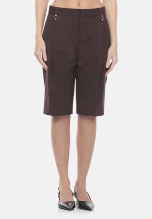 Donna che indossa pantaloncini sartoriali marroni scuri al ginocchio con pieghe e tacchi slingback neri a punta.