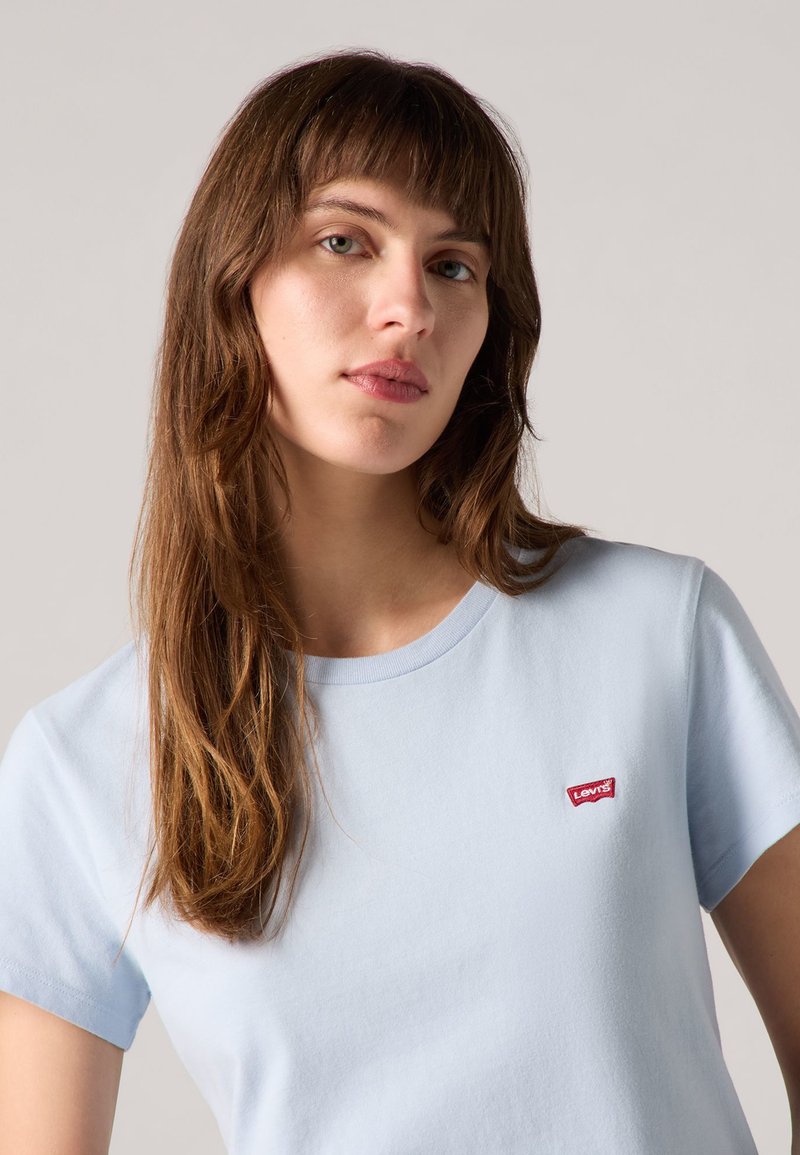 Camiseta de algodón de manga corta en azul claro, con un escote redondo y un pequeño logotipo rojo de Levi's en el lado izquierdo del pecho. Textura suave.
