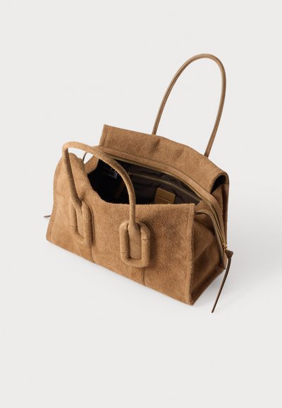 Sac à main en daim marron avec deux poignées, fermeture éclair partiellement ouverte montrant l'intérieur sombre et les compartiments intérieurs sur fond blanc.