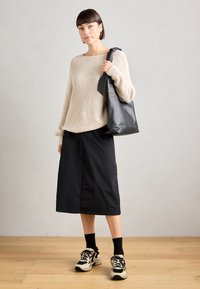 Beige ribbed sweater, black knee-length skirt, and black leather bag. Model wears black socks and beige sneakers with black accents.