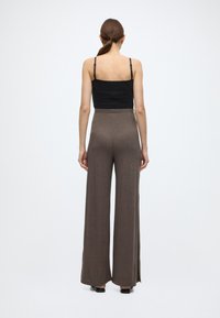 Μαύρο εφαρμοστό αμάνικο τοπ με ρυθμιζόμενους ιμάντες ώμων, συνδυασμένο με ψηλόμεσο, καφέ παντελόνι με φαρδιά μπατζάκια και πλαϊνές σχισμές.