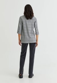 Blazer gris à carreaux avec manches trois-quarts, associé à un pantalon droit gris foncé et des chaussures noires. Tissu lisse avec une texture subtile.