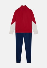 Sarkana un balta sporta jaka ar augstu apkakli un garām piedurknēm, savienota ar tumši ziliem biksēm. Gluda auduma, sportisks piegriezums un ribotas piedurknes.