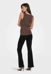 Bruine mouwloze top met een aansluitend ontwerp, gecombineerd met zwarte flared jeans. Het model staat zijwaarts, toont een eenvoudige silhouet en een zachte textuur.