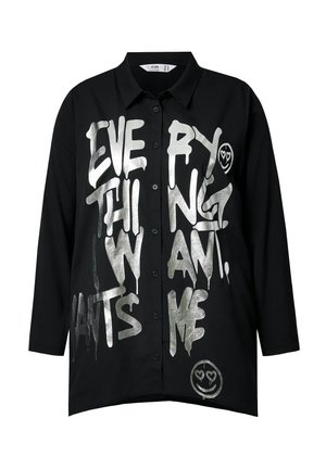 Chemise noire à boutons avec du texte en style graffiti argenté disant "TOUT CE QUE JE VEUX", accompagnée d'un graphique de smiley. Manches longues, coupe décontractée.