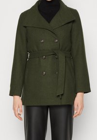 Abrigo de mezcla de lana en verde oliva, con un amplio cuello, botones de doble botonadura, cintura ceñida con cinturón y mangas largas. Tela texturizada y dos bolsillos.