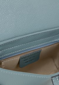 Hellblaues Lederhandtasche mit texturierter Oberfläche. Verfügt über einen Reißverschluss, beiges Innenfutter und ein Innenetikett, das "Echtes Leder Made in Italy" besagt.