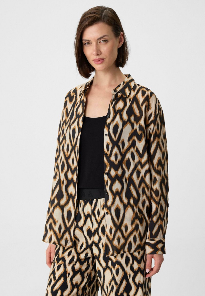Losse, knoop-overshirt van een gladde stof met een gedurfde luipaardprint in schakeringen van zwart, bruin en beige. Zwarte tanktop eronder.