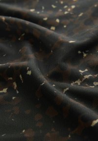 Sort stof med fin mesh-struktur og uregelmæssige brune og beige pletter, der viser naturlige folder og en let glans under lys.