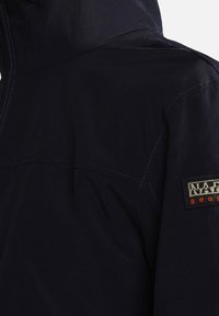 Chaqueta impermeable de color navy con capucha, costuras visibles y un parche de tela con el nombre de la marca "Napapijri" en acentos rojos y blancos.