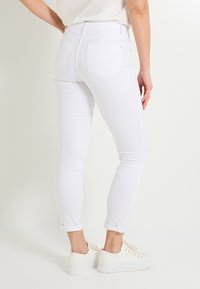 Vaqueros blancos ajustados con una cintura alta, puños enrollados y dos bolsillos traseros. La tela parece elástica y suave. Combinados con zapatillas blancas.