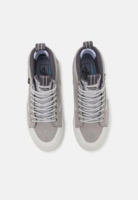 Zapatillas altas de ante gris claro con suelas de goma blanca, puntera redonda, cordones grises y cuello acolchado; presenta un logo y acentos multicolor.