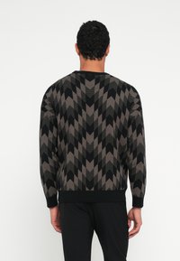 Czarny i brązowy sweter w wzór szewronu, z okrągłym dekoltem i ściągaczami na mankietach, widoczny od tyłu.