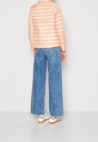 Jasnoróżowa kurtka puchowa o krótkim kroju, z prążkowanym kołnierzem i pikowaną fakturą, zestawiona z szerokimi niebieskimi dżinsami i białymi tenisówkami.