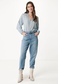 Blusa azzurro chiaro con scollatura a V e dettagli arricciati, abbinata a jeans di denim chiaro a vita alta e stivaletti beige con tacco quadrato.