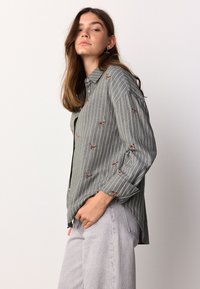 Green and white striped button-up shirt with small embroidered details. Long sleeves, collared design, and a relaxed fit.