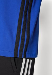 Blauwe T-shirt met een zwart drie-strepenontwerp langs de zijkanten, gemaakt van een soepel katoenmateriaal, met een rechte zoom en korte mouwen.