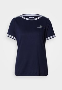 T-shirt bleu marine avec texture côtelée, accents à rayures blanches sur le col et les manches, et petit logo vert Lacoste sur la poche.