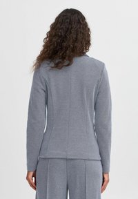 Grå långärmad topp med en figursydd design, texturerat tyg och en sömdetalj som löper längs ryggen. Inga synliga knäppningar eller dekorationer.