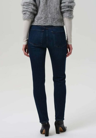 Jean en denim skinny bleu foncé, doté d'un design à cinq poches, de coutures discrètes et de détails au niveau de l'empiècement arrière, associé à un pull léger.