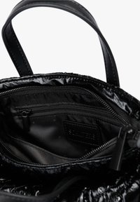 Interior de un bolso de mano negro brillante mostrando un bolsillo con cremallera, una etiqueta de tela y una correa para el hombro sobre un fondo blanco.