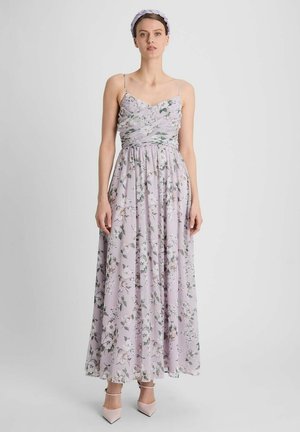 Femme portant une robe longue sans manches à fleurs lavande avec un bandeau assorti et des talons pointus rose pâle.