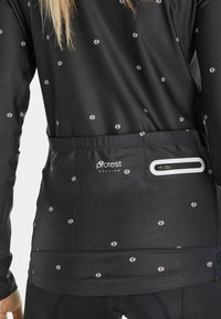 Black cycling jersey with pink and white floral patterns, a fitted design, and a zippered pocket at the back. Made from smooth, stretchy fabric.