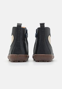 Bottines en cuir noir avec une finition texturée, accents beiges, zips sur le côté et semelles en caoutchouc marron. Détails surpiqués le long des bords.