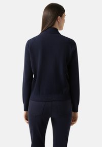 Granatowy sweter dzianinowy z prążkowanym kołnierzem i długimi rękawami. Gładka faktura i dopasowany krój, zestawiony z ciemnymi spodniami.