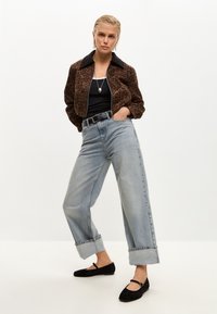 Chaqueta de estampado de leopardo, top negro sin mangas, jeans de pierna ancha azul claro con puños doblados y bailarinas de ante negras. Incluye collar con colgante de plata.