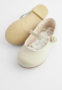 Zapatos Mary Jane en color beige brillante con una correa brillante, plantilla floral y suela de goma que presenta motivos decorativos de zapatillas de ballet.