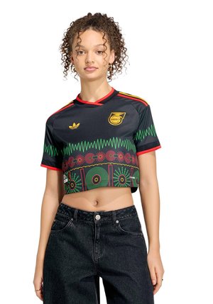 Naiste lokkis juustega, kandes musta lühikest Jamaica jalgpallipluusi punaste, kollaste ja roheliste mustritega ning kõrge vöökohaga musti teksaseid.