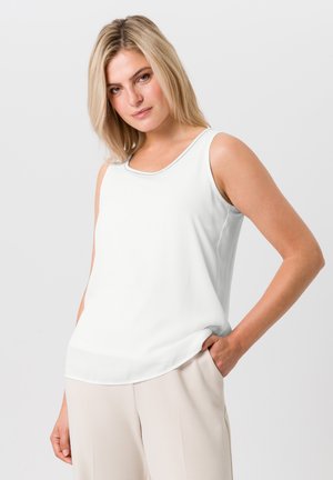 Haut sans manches blanc avec un col rond, texture lisse et subtile brillance ; associé à un pantalon beige clair.