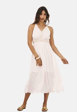 Vestido blanco sin mangas con un corpiño ajustado y cintura imperio. Presenta costuras decorativas a lo largo del escote. Tejido largo hasta el suelo y fluido.