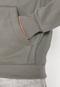 Felpa grigia con tasca a marsupio, polsini a coste e cuciture decorative lungo le cuciture. Tessuto morbido con una vestibilità rilassata.