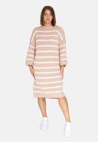 Strickkleid mit blassrosa und weißen Streifen, übergroßen Ärmeln und geradem Schnitt, kombiniert mit weißen Schuhen.