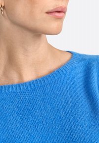 Maglione blu a maglia con un ampio scollo a coste. La texture è morbida, realizzata in un materiale leggero e leggermente peloso.