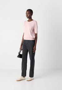 Light pink short-sleeve sweater, paired with black high-waisted jeans, and beige sneakers. Model holds a small black handbag.
