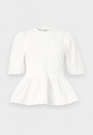 Fehér blúz pöndörödő könyékig érő ujjakkal, ráncolt derékkal és hullámos szegéllyel az ujjakon és az alján, egyszínű háttéren bemutatva.