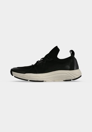 Sort lav sneaker med hvidt struktureret sål, strikket overdel, trækstrop ved hælen og snørelukning foran på ensfarvet baggrund.