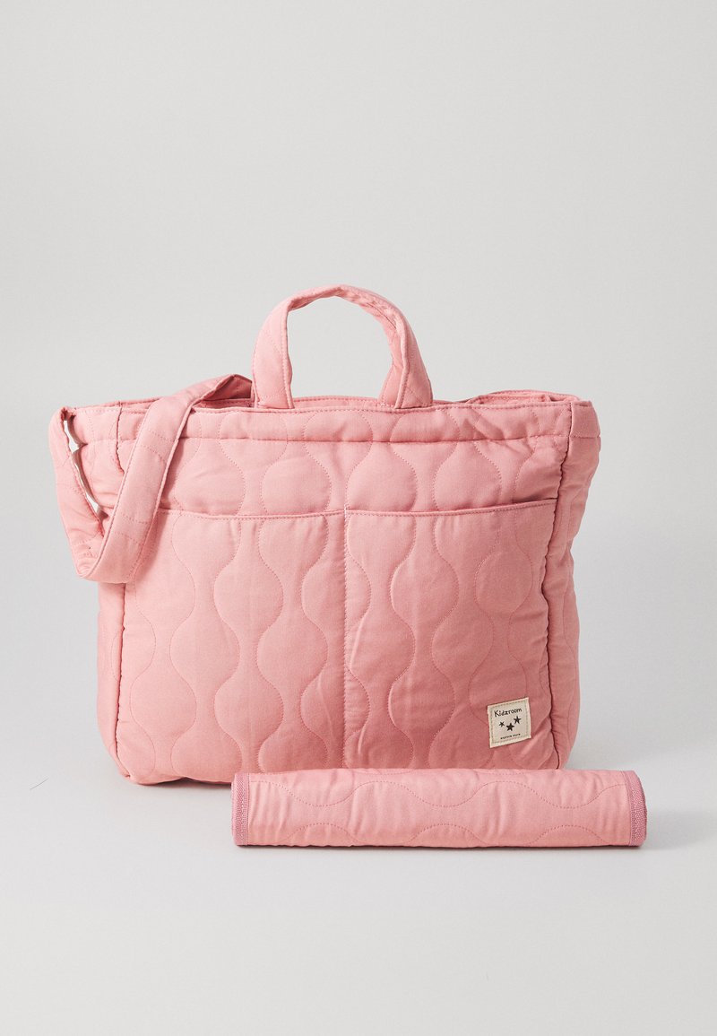 Tote torba iz pikastega roza blaga z dvema ročajema in naramnim trakom; ima gladko teksturo in žep na sprednji strani. Vključuje zvit dodatni del.