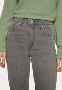 Grå höga jeans i denim, med knappstängning, framfickor och subtila sömnadsdetaljer. Stylade med en grön tröja.