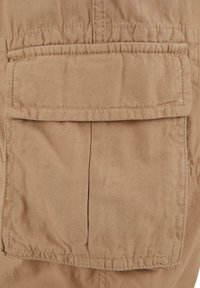 Tan fabric pocket with a flapped closure, stitched edges, and a smooth texture, part of a garment's front panel.
