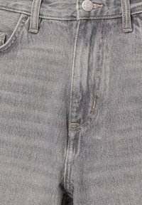 Gros plan sur l'avant d'un jean en denim gris avec passants de ceinture visibles, bouton en métal et rivets de poche.