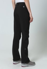 Pantalones exteriores negros de corte recto, con cintura elástica, acentos reflectantes y cremalleras en los tobillos. Combinados con zapatillas deportivas grises.