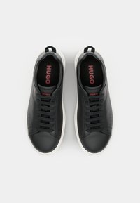 Czarne skórzane sneakersy z białymi podeszwami, kontrastującym czerwonym logo na języku oraz sześcioma czarnymi oczkami na sznurówki. Gładka tekstura z minimalistycznym wzorem.