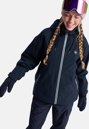 Black insulated jacket with white zipper accents, paired with black gloves. The model wears a light purple beanie and ski goggles with reflective lenses.