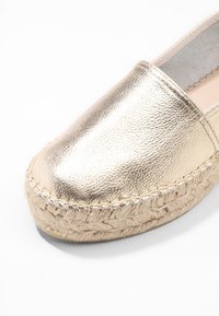 Espadrillas in pelle dorata con punta arrotondata, suola in corda di juta e dettagli intrecciati attorno ai bordi, caratterizzate da un finish metallico testurizzato.