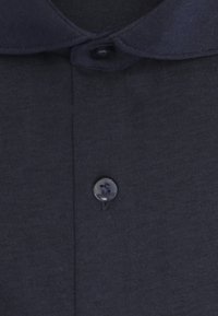 Col de chemise bleu marine foncé avec un bouton fermé et un autre bouton visible en dessous sur un tissu lisse.
